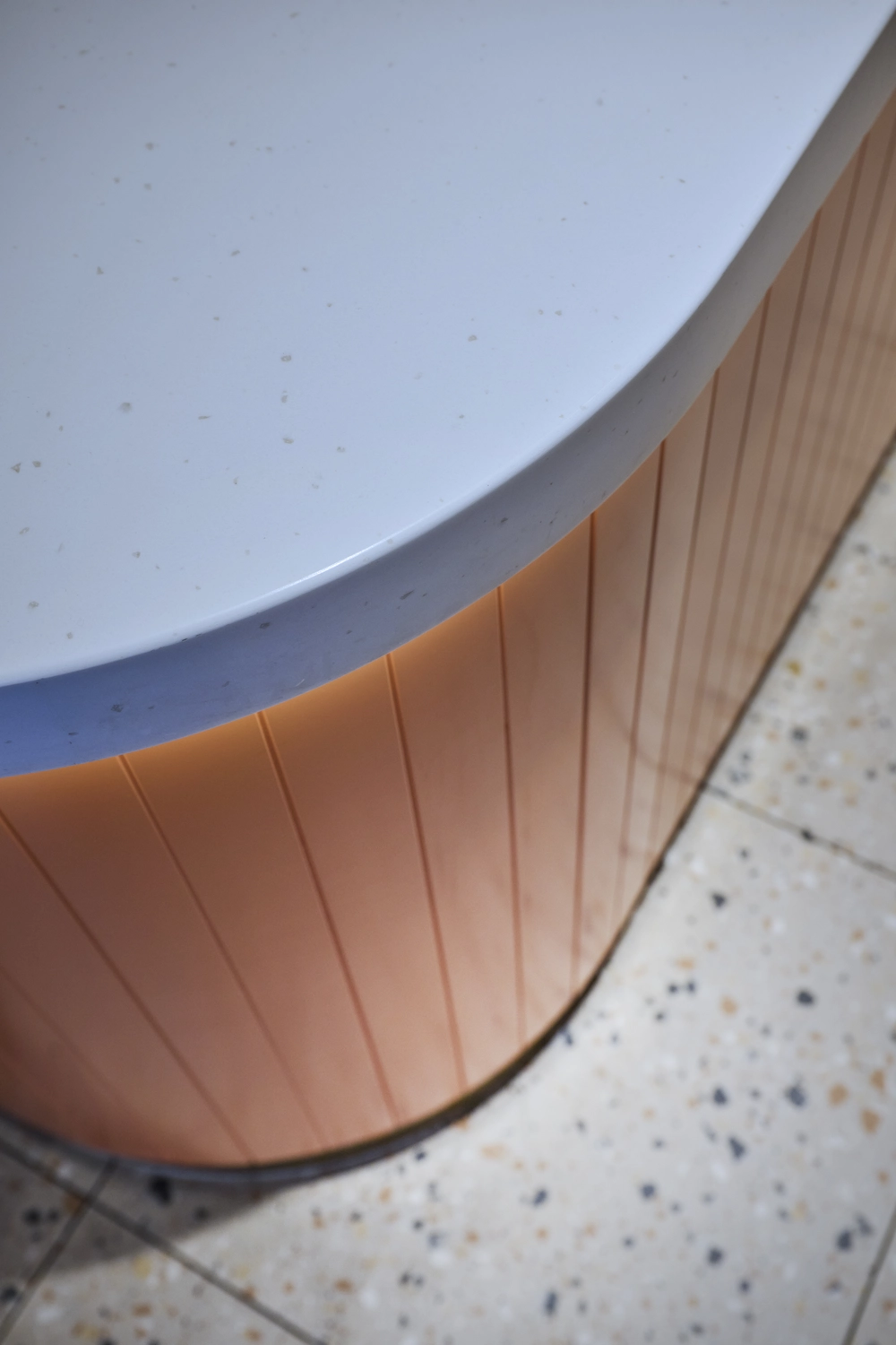 Heinrich Buchholz-Holzbearbeitung-Modernes Café-Interieur mit hellblauer vertikaler Lamellen-Servicetheke, dunkler Marmorarbeitsplatte und warmer LED-Basisbeleuchtung, vor einer dunkelgrünen Wand und einer maßgefertigten, passenden Tür mit rundem Bullaugenfenster.