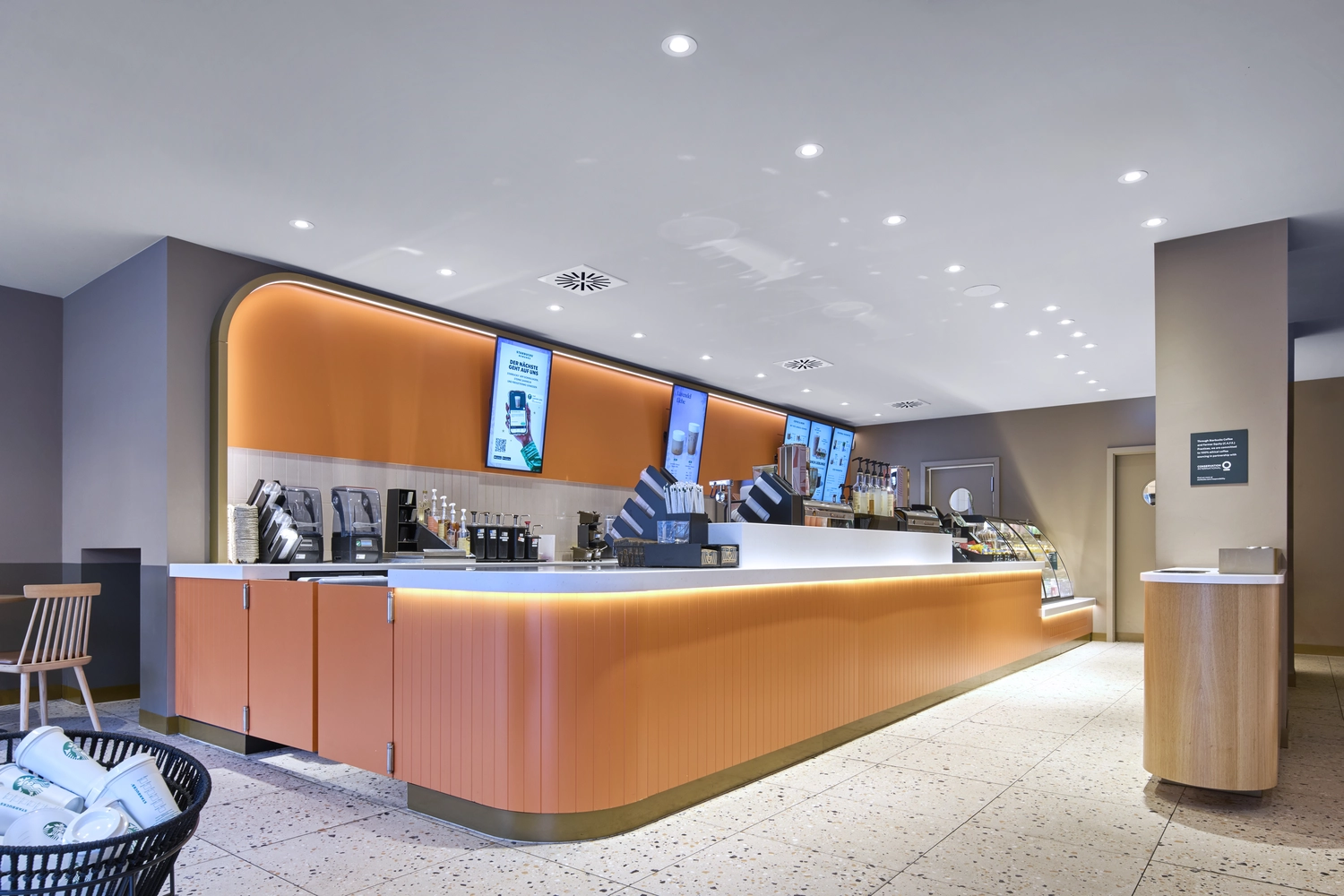 Heinrich Buchholz – Holzbearbeitung – Moderne Ladenfront eines Geschäftsgebäudes mit einem Starbucks-Café, großen Glasfronten, elegantem schwarzem Holzrahmen und gepflastertem Außenbereich.