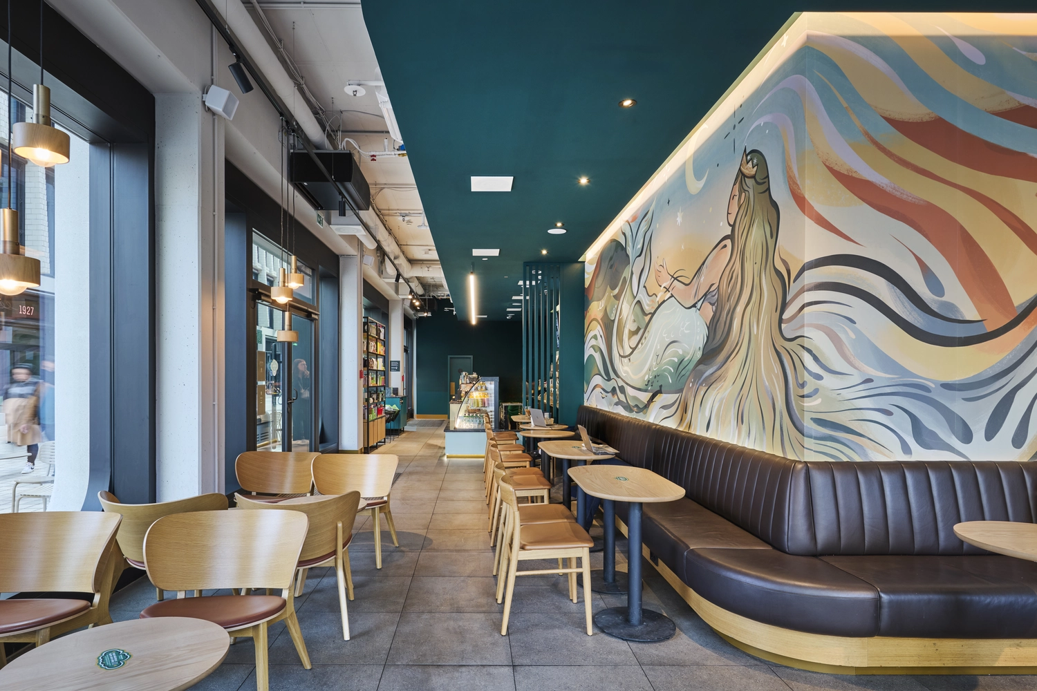 Heinrich Buchholz - Holzbearbeitung - Modernes Café-Interieur mit individuell gebogenen Holzstühlen und -tischen, einer geschwungenen Ledersitzbank mit Holzsockel und einem lebhaften Meerjungfrauen-Wandbild.