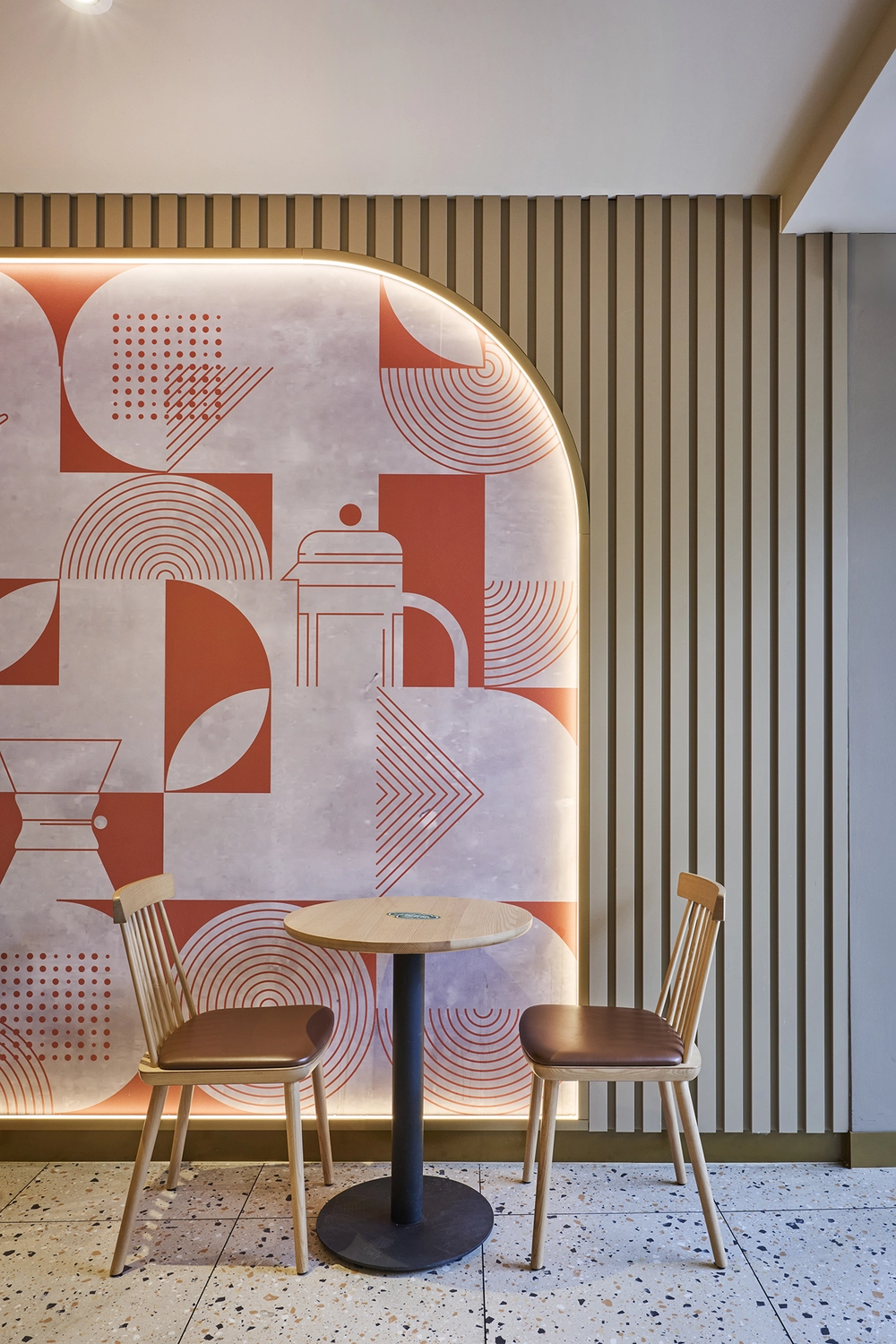 Heinrich Buchholz-Holzbearbeitung-Modernes Café-Interieur mit hellblauer vertikaler Lamellen-Servicetheke, dunkler Marmorarbeitsplatte und warmer LED-Basisbeleuchtung, vor einer dunkelgrünen Wand und einer maßgefertigten, passenden Tür mit rundem Bullaugenfenster.