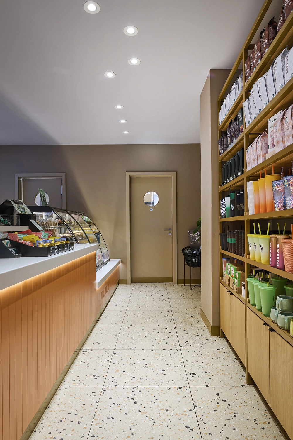 Heinrich Buchholz-Holzbearbeitung-Modernes Café-Interieur mit hellblauer vertikaler Lamellen-Servicetheke, dunkler Marmorarbeitsplatte und warmer LED-Basisbeleuchtung, vor einer dunkelgrünen Wand und einer maßgefertigten, passenden Tür mit rundem Bullaugenfenster.