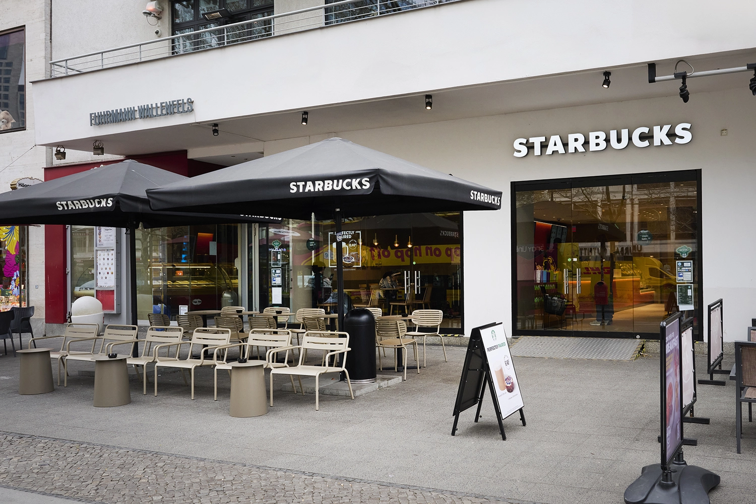Heinrich Buchholz-Holzbearbeitung-Modernes Café-Interieur mit hellblauer vertikaler Lamellen-Servicetheke, dunkler Marmorarbeitsplatte und warmer LED-Basisbeleuchtung, vor einer dunkelgrünen Wand und einer maßgefertigten, passenden Tür mit rundem Bullaugenfenster.