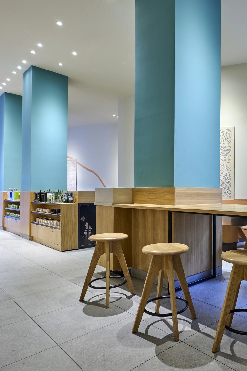 Heinrich Buchholz – Holzbearbeitung – Moderne Café-Theke mit geschwungener Fassade aus Naturholzlatten und warmer LED-Unterbaubeleuchtung vor einer türkisfarbenen, geriffelten Akzentwand.
